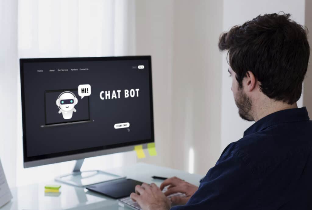 Homme devant un ordinateur. Sur l'écran, un chatbot